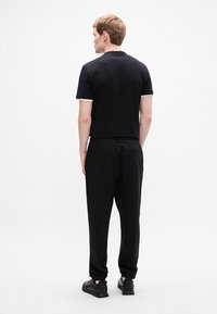 Männliches schwarzes T-Shirt und Jogginganzug. Das T-Shirt hat einen runden Halsausschnitt mit weißem Saum. Die Jogginghosen haben einen elastischen Bund und eng zulaufende Bündchen.