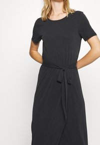 Musta jersey-mekko, jossa on lyhyet hihat, pyöreä kaula-aukko ja vyötärösolmimus. Mekko on rento istu ja siinä on sileä rakenne.