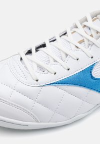 Scarpa sportiva bianca con texture trapuntata, accento blu e lacci standard. Presenta una parte superiore liscia e un pannello laterale testurizzato per la presa.