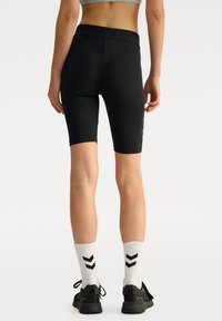 Czarne rowerowe szorty z wysokim stanem, o gładkiej fakturze i dopasowanym kroju, zestawione z białymi skarpetkami w czarny wzór w zygzak i czarnymi sneakersami.