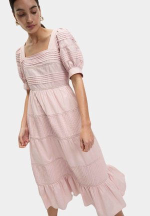Pink kjole med firkantet udskæring, puffede ærmer og lagdelt design. Har tekstureret panelering og flæsekant for ekstra detaljer.