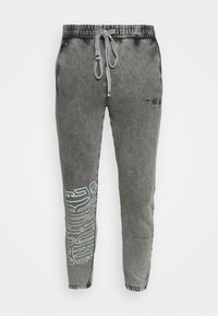 Šedé joggingové kalhoty vyrobené z jemné, texturované tkaniny. Obsahují elastický pas se šňůrkou a bílý grafický potisk na nohavici.