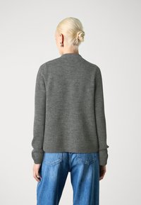 Grauer Strickpullover mit rundem Halsausschnitt und gerippten Bündchen, kombiniert mit hellblauen, hochgeschnittenen Jeans mit Gesäßtaschen.