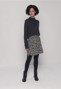 Pull gris en maille, jupe à motif léopard, leggings noirs et bottines. Texture lisse avec un design à couches sur la jupe.