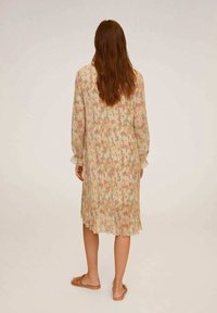 Blumendesignet, plissiertes Midi-Kleid aus weichem Stoff, mit langen Ärmeln und einem Rüschensaum. Erdtöne dominieren das Design.