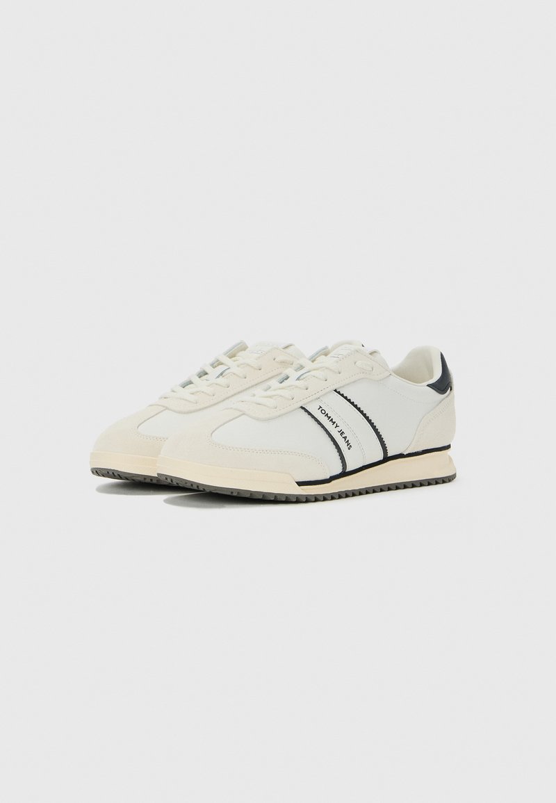 Baskets basses crème avec des rayures noires, logo "TOMMY JEANS" sur les côtés, fermeture à lacets et semelle beige striée.