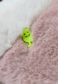 Tejido de felpa difusa en tonos blancos y rosas, con una pequeña figura de un fantasma sonriente verde parcialmente visible entre las fibras.