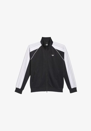 Chaquetas de pista en blanco y negro con cremallera, cuellos altos y acentos a rayas. Pantalones negros, camisetas blancas debajo. Tejido texturizado.