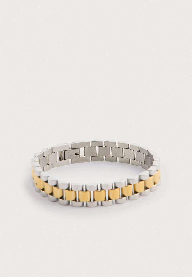 Metalen armband met afwisselende zilveren en gele schakels, met een ronde vorm en een veilige sluiting. Het oppervlak heeft een gladde textuur.