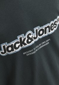 Ciemnozielona bawełniana koszulka z dużym białym i czarnym napisem "Jack&Jones" oraz mniejszym napisem "dostarczone przez ORG DEPT. ZAPROJEKTOWANE W KOPENHADZE."