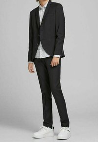 Mörkgrå kostym med strömlinjeformad design, kombinerad med en vit mönstrad skjorta och vita sneakers, med smala byxor och en kavaj med enkelknäppning.