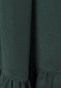 Tessuto verde scuro con trama e dettagli arricciati o plissettati vicino al bordo inferiore, creando pieghe morbide.