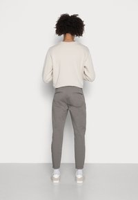 Sweat-shirt gris clair à manches longues, associé à un pantalon gris resserré aux chevilles. La tenue est complétée par des chaussettes blanches et des baskets beiges.
