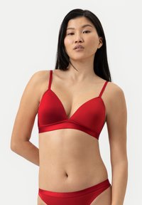 Punainen kolmion muotoinen rintaliivih brasetti säädettävillä säärillä, sileää kangasta ja leveä satiininen vyö rinnan alta. Yhdistettynä matchaaviin punaisiin alushousuihin.