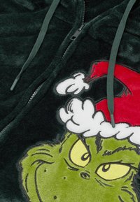 Zielona pluszowa bluza z kapturem na zamek błyskawiczny. Z przodu duża grafika Grincha z żółtymi oczami i czerwonym kapeluszem Świętego Mikołaja, ozdobiona białym futerkiem.