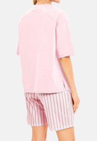 Ljusrosa bomulls t-shirt med kort ärm och avslappnad passform, kombinerad med rosa och vita vertikala randiga shorts. Sidofickor på t-shirten.