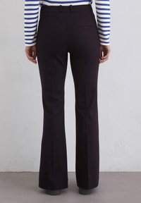 Czarne spodnie dzwony uszyte z materiału o gładkiej fakturze. Posiadają kieszeń z tyłu i dziurki na pasek, noszone z prążkowaną bluzką z długim rękawem.
