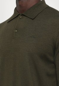 Oliwkowa koszulka polo wykonana z teksturowanej dzianiny, z kołnierzykiem, dwoma guzikami i małym logo nadrukowanym na klatce piersiowej.
