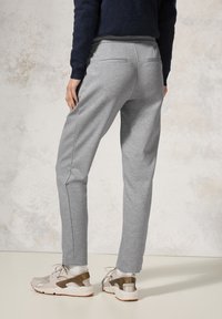 Ljusgrå sweatpants med en tapered design, elastisk midjeband och diskreta bakfickor, i kombination med beige och bruna sportskor.