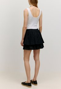 Zwarte gelaagde mini-jurk met een gestructureerde stof, gecombineerd met een witte mouwloze top. De rok heeft een elastische tailleband en gelaagde volants.