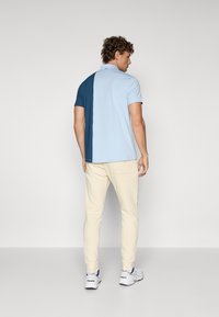 Short-sleeve polo shirt featuring a split design in light blue and dark blue, made of soft fabric. Paired with cream-colored pants and white shoes.