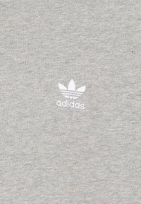 Ljusgrå bomulls-T-shirt med en liten vit Adidas-logotyp med trebladsmönster. Texturen är mjuk med ett subtilt melerat mönster.