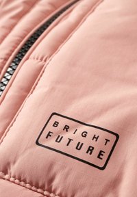 Section de veste matelassée rose avec fermeture éclair noire et texte noir "BRIGHT FUTURE" imprimé à l'intérieur d'un contour rectangulaire.