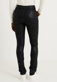 Pantalon en similicuir noir avec un motif texturé effet peau de serpent, coupe ajustée et poches arrière, assorti à des baskets blanches.