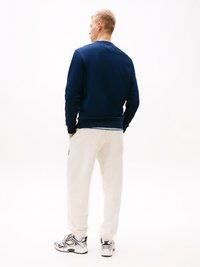 Sweatshirt azul-marinho com tecido texturizado, combinado com calças de sweat crème. Ténis brancos com detalhes em preto e cinza. Design simples e casual.