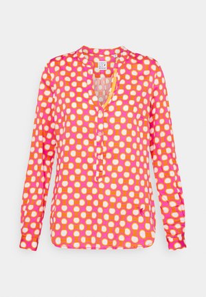 Langærmet lyserød bluse med orange og hvidt cirkulært geometrisk mønster og en delvis knaplukning foran.