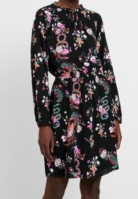 Černé šaty s květinovými vzory v růžové a zelené barvě, dlouhými rukávy, kulatým výstřihem se šněrováním a elastickým pasem.