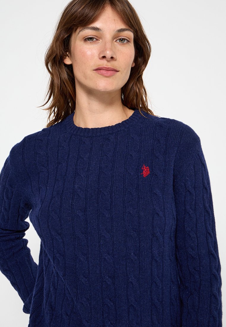 Marineblauer Kabelstrickpullover aus weichem Material, mit Rundhalsausschnitt und kleinem roten Logoakzent auf der Brust.
