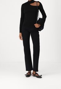 Schwarzes Langarmoberteil mit Cut-Out-Detail, kombiniert mit schwarzen geraden Jeans und flachen schwarzen Schuhen mit Riemen. Einfaches Design und Texturen.