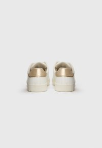 Weiße Sneaker mit glatter Textur, die an der Ferse mit einem metallischen goldenen Akzent versehen sind, und Gummisohlen für besseren Halt.