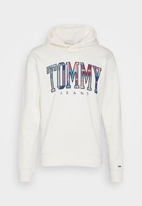 Krémová mikina s kapucí vyrobená z bavlněného směsového materiálu, s velkým grafikou "TOMMY JEANS" v mnoha barvách. Obsahuje přední klokaní kapsu a nastavitelnou kapuci se stahovací šňůrkou.