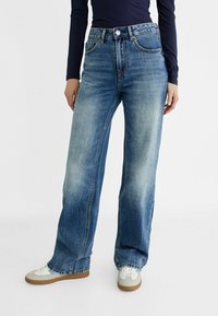 Light blue denim wide-leg jeans with a high waist, featuring subtle faded areas, five-pocket design, and metal button closure.