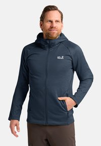 Giacca leggera di colore blu scuro con cappuccio, chiusura frontale con zip e tasche laterali. Presenta un tessuto texture e un piccolo logo sul petto.