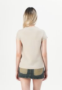 Beige fitted t-shirt with short sleeves, featuring a crew neck. Paired with a green denim mini skirt with dual-tone pockets and frayed hem.
