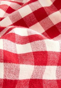 Rot-weiß kariertes Gewebe mit einer weichen, strukturierten Oberfläche. Das Muster zeigt abwechselnde Quadrate mit Fischgrätenmustern in helleren Schattierungen.