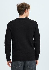 Svart ribbat stickat tröja med långa ärmar och rundad halsringning, med en något lös passform och mjuk textur, sedd från baksidan.