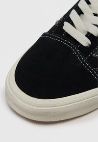 Adidași negri din suede, cu vârf rotunjit, șireturi albe și talpă din cauciuc texturat. Prezintă cusături albe de-a lungul marginii.