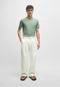 Groene t-shirt met korte mouwen, gecombineerd met witte, wijde broek en bruine sandalen met een gesp. Eenvoudig ontwerp, zachte stoffen en neutrale kleuren.