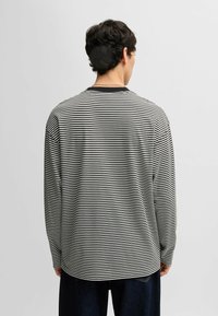 Svartvit randig långärmad topp med rundad halsringning och lös passform, visad bakifrån.