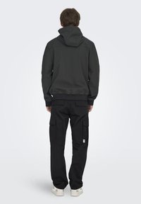 Donkergrijze hoodie met een gladde textuur, gecombineerd met zwarte cargobroeken met meerdere zakken en een logo-label op het been.