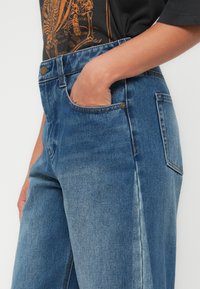 Lichte blauwe denim jeans met een relaxte fit, voorzien van een hoge taille, zijzakken en een zichtbaar metalen knoopdetail op de tailleband.