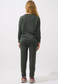Dunkelgrüner Strickpullover und passende Jogginghose mit lockerer Passform und weichem Material. Tragen mit lila und grauen Sportschuhen.