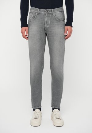 Jeans in denim grigio con una vestibilità slim, caratterizzati da un design tradizionale a cinque tasche, chiusura frontale con bottone e leggera scoloritura. Indossati con sneakers beige.