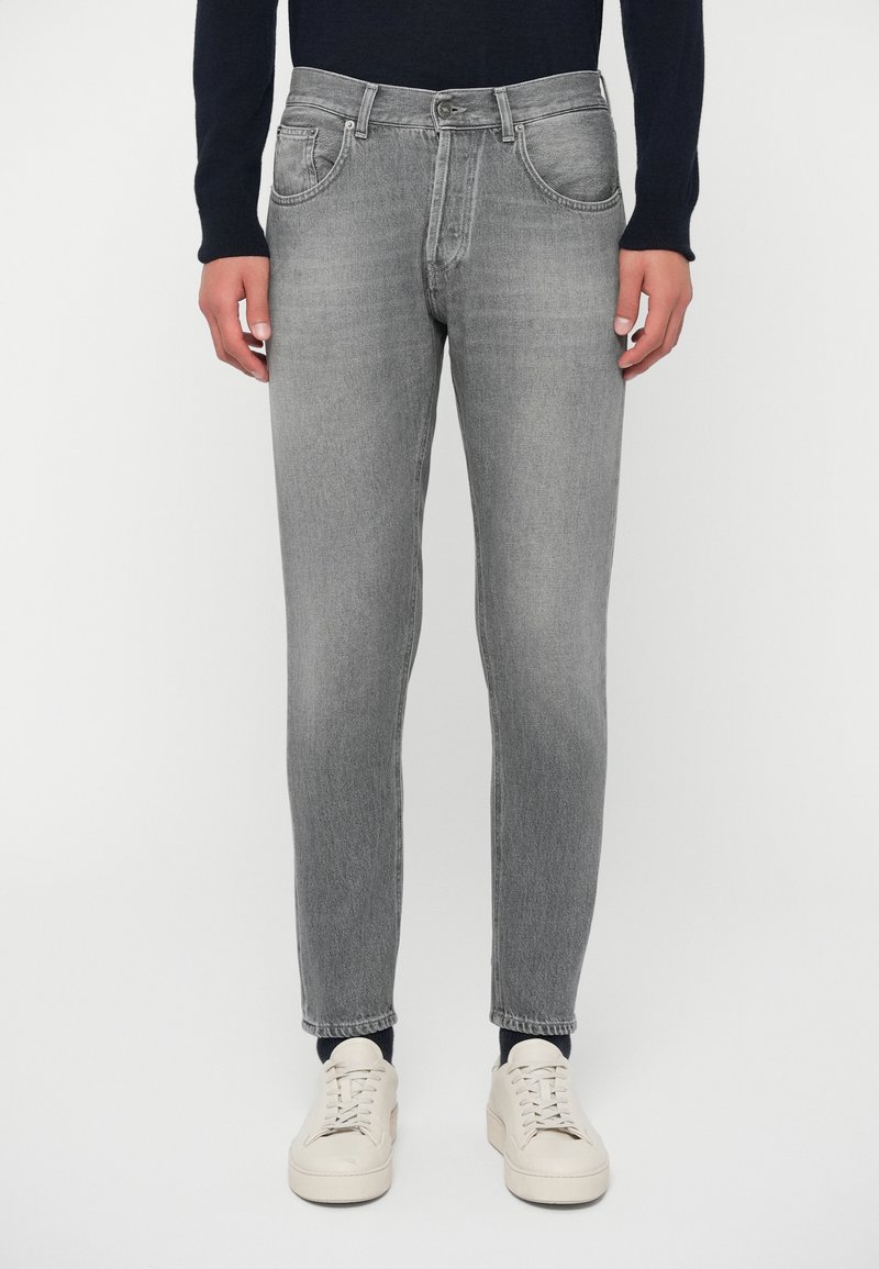 Γκρι τζιν παντελόνι με στενή γραμμή, διαθέτει παραδοσιακό σχέδιο πέντε τσεπών, μπροστινό κούμπωμα με κουμπί και ελαφριά ξεθώριασμα. Φοριέται με μπεζ αθλητικά παπούτσια.