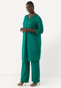 Teal tvådelad outfit med en lång tunika med V-ringning och trekvartsärmar, kombinerad med vida byxor och sandaletter.