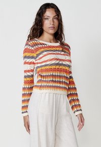 Suéter de ganchillo con vibrantes rayas en naranja, rojo y gris, con una textura de punto y mangas largas, terminado con un dobladillo color crema.